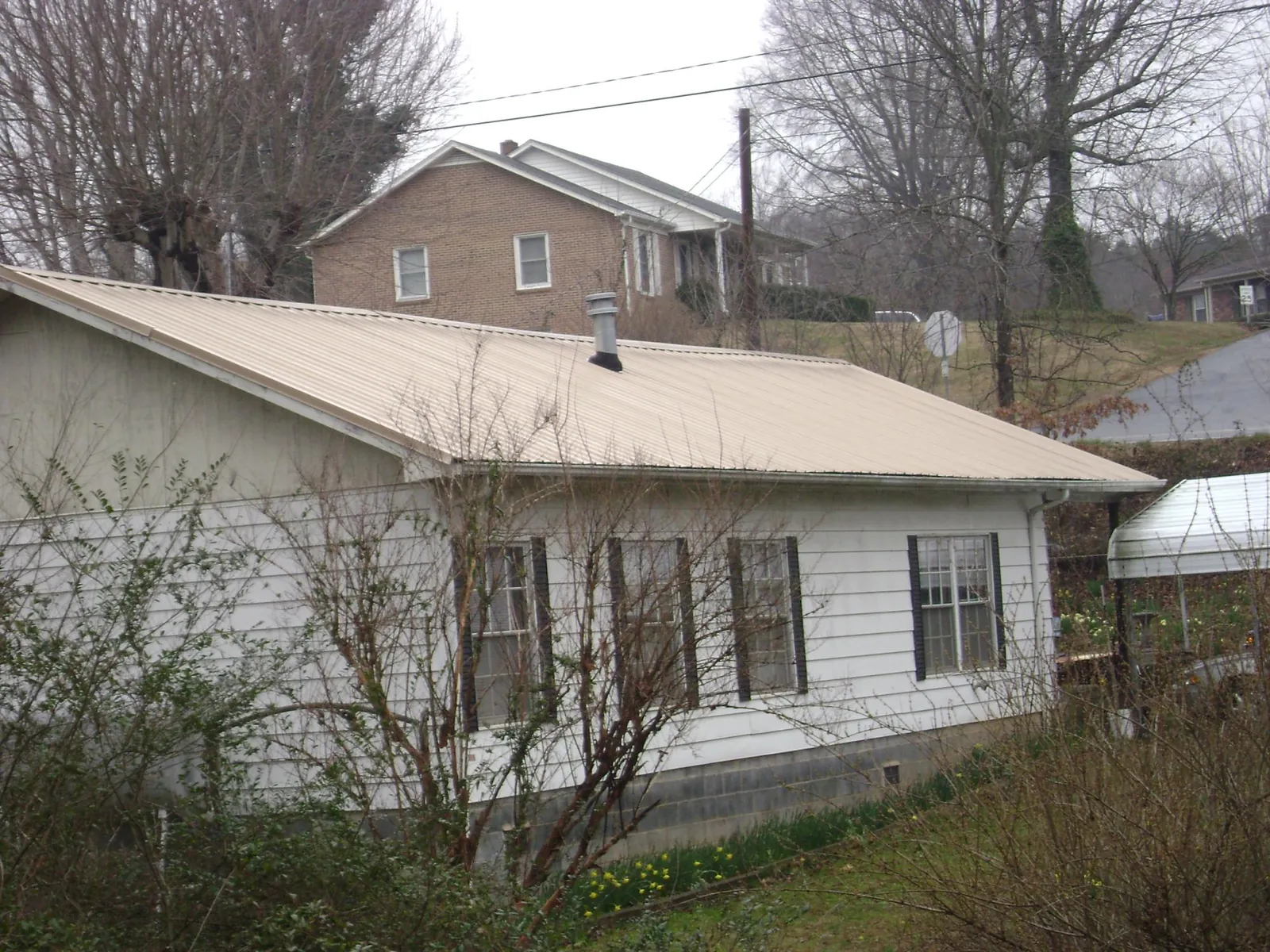 Tan metal roof on a white sided house set into a hillside — Commercial Roofing by Roofing Brothers in Delray Beach