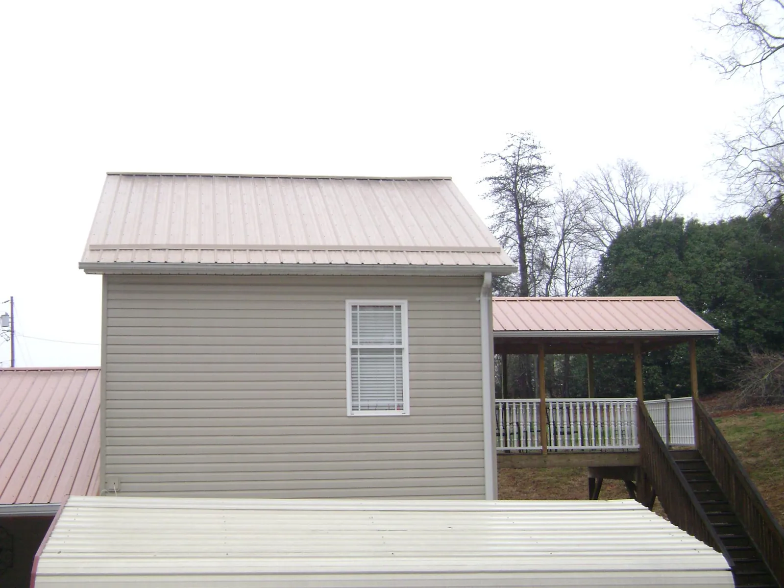 Tan metal roofs on a two story addition and attached porch, from a Roof Replacement job in Delray Beach